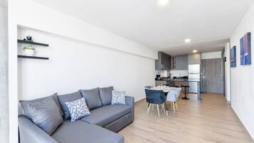 A modern living room with a grey sectional sofa, a dining table with chairs, and a kitchen in the background.