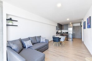 Una sala de estar moderna con un sofá seccional gris, una mesa de comedor con sillas y una cocina al fondo.