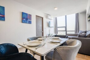 Una sala de estar moderna con una mesa de comedor preparada para dos personas, un sofá y un televisor montado en la pared.