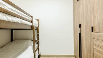Een stapelbed met een houten trap, een kast met zwarte handgrepen en een betegelde vloer.