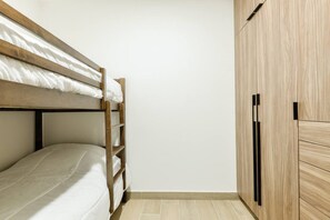 Un lit superposé avec une échelle en bois, une armoire avec des poignées noires et un sol carrelé.