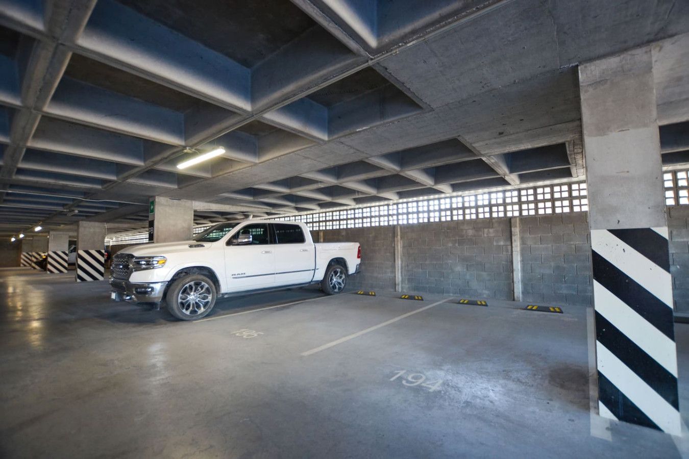 A white pickup truck parked in a multi-level underground parking garage with concrete pillars and striped safety barriers.