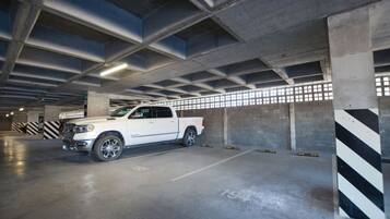 A white pickup truck parked in a multi-level underground parking garage with concrete pillars and striped safety barriers.