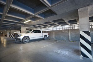 Un camionnette blanche était garée dans un parking souterrain à plusieurs niveaux, avec des piliers en béton et des barrières de sécurité rayées.