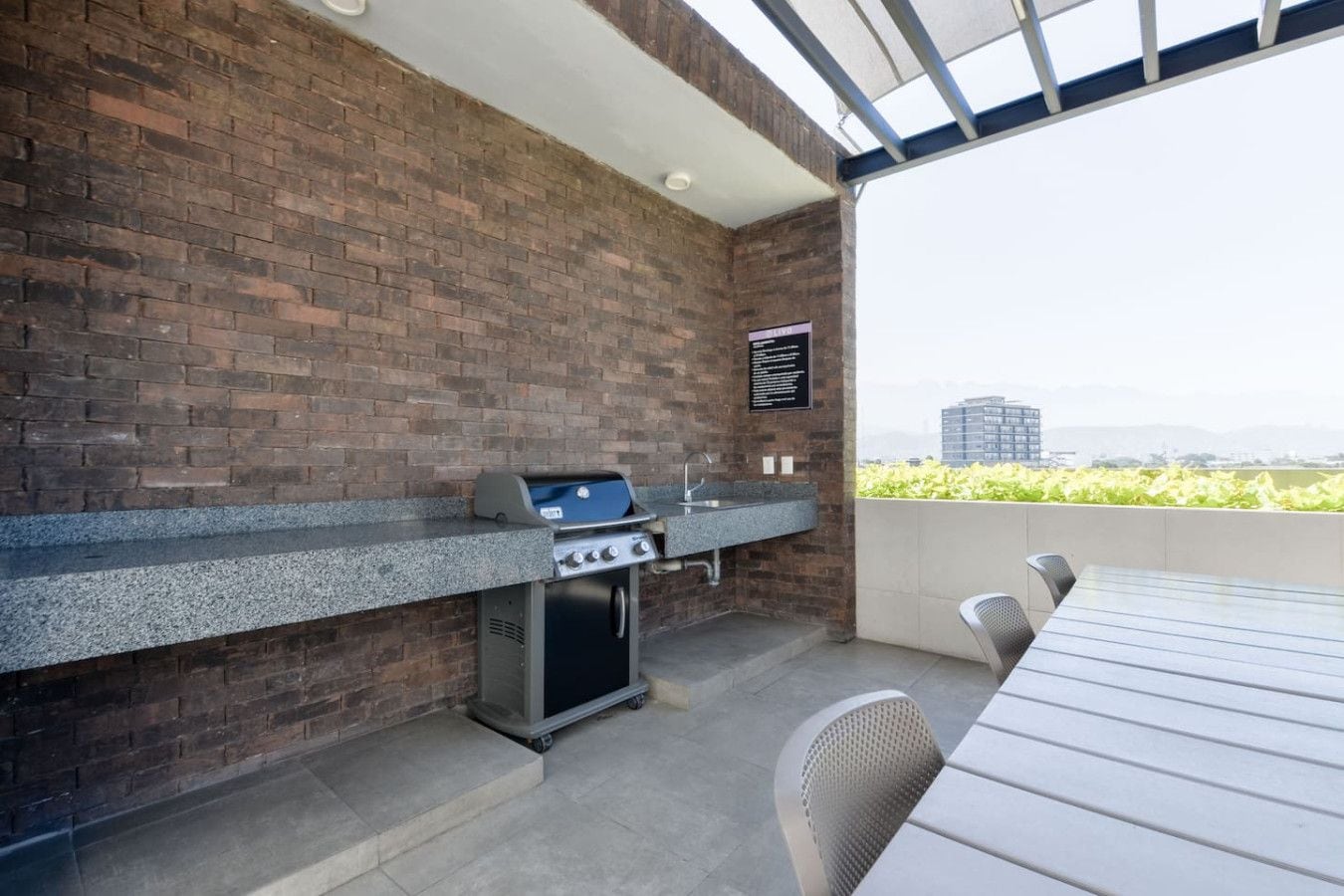 An outdoor kitchen with a brick wall, a gas grill, a sink, and a table with chairs.