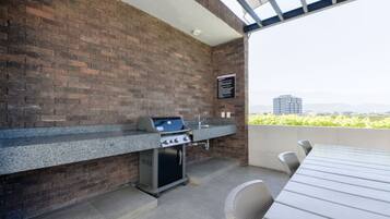 An outdoor kitchen with a brick wall, a gas grill, a sink, and a table with chairs.