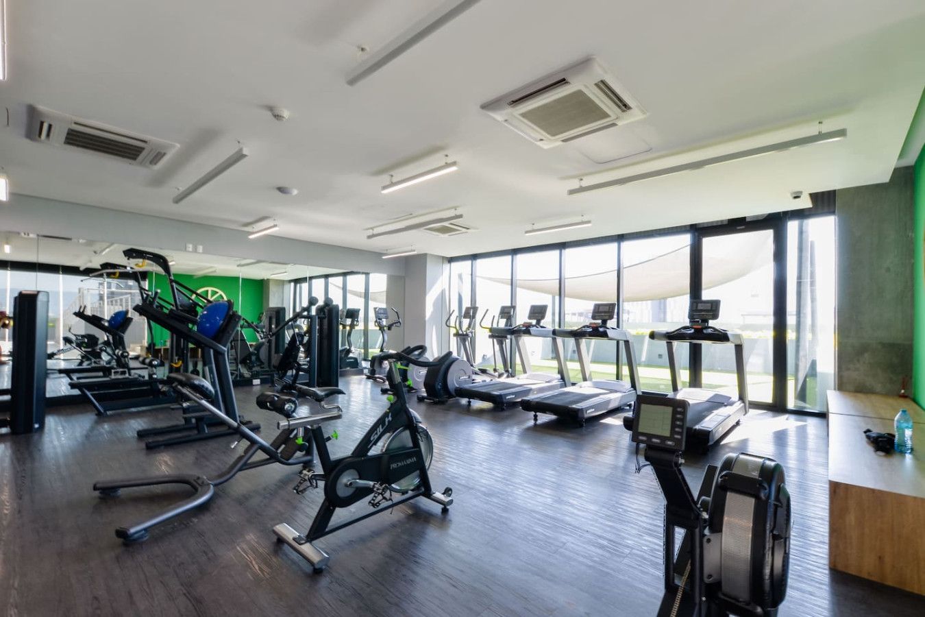 A spacious gym with various exercise equipment, large windows, and a modern design.