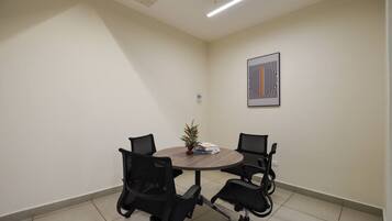A conference room with a round table, four black office chairs, a small plant, and a framed abstract artwork on the wall.