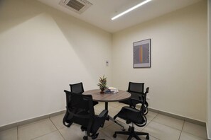 Un salón de conferencias con una mesa redonda, cuatro sillas de oficina negras, una planta pequeña y una obra de arte abstracta enmarcada en la pared.
