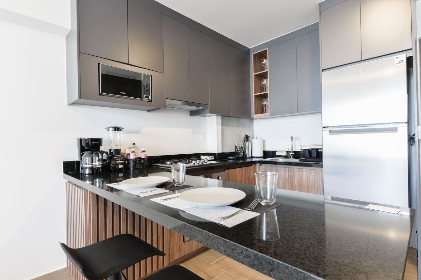 A modern kitchen with grey cabinets, a stainless steel refrigerator, a microwave, and a coffee maker.