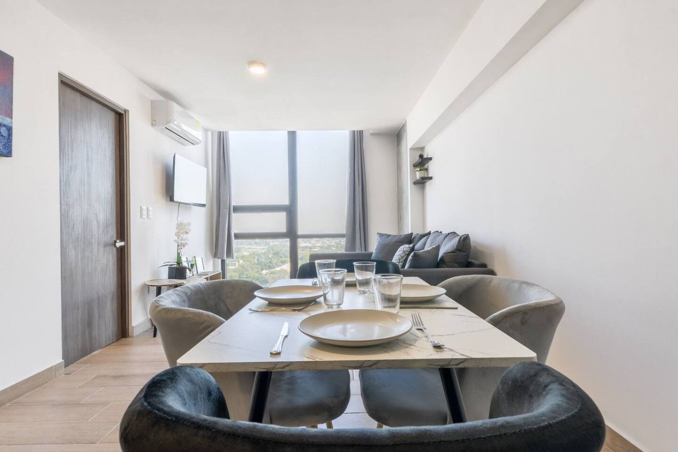 A dining area with a table set for four, a sofa, and a large window offering a view.