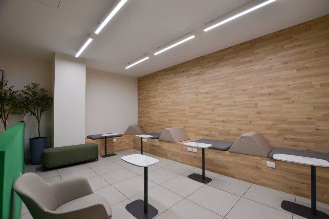 A modern waiting area with a wooden wall, green seating, and tables.