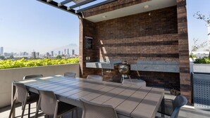 Een terras buiten, met een bakstenen muur, een barbecue en een tafel met stoelen.