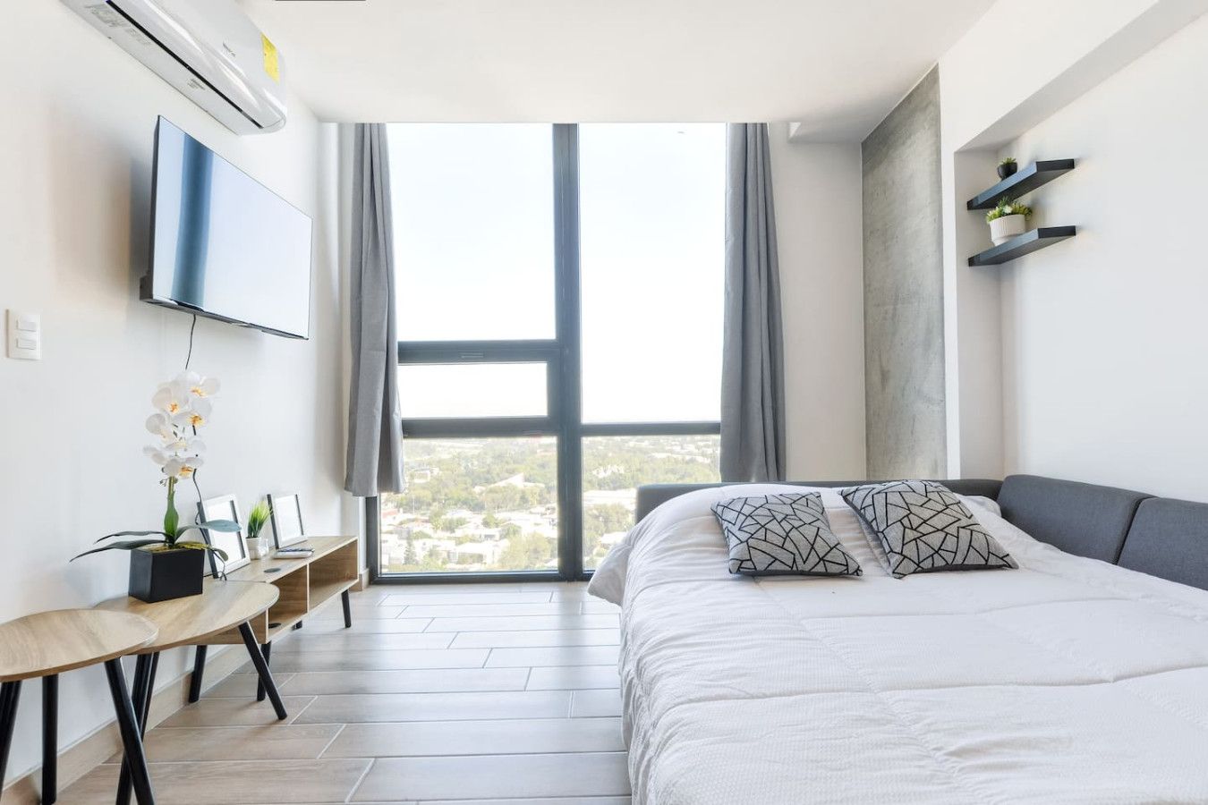 A modern bedroom with a large bed, a desk, and a TV mounted on the wall.