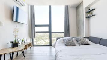 A modern bedroom with a large bed, a desk, and a TV mounted on the wall.