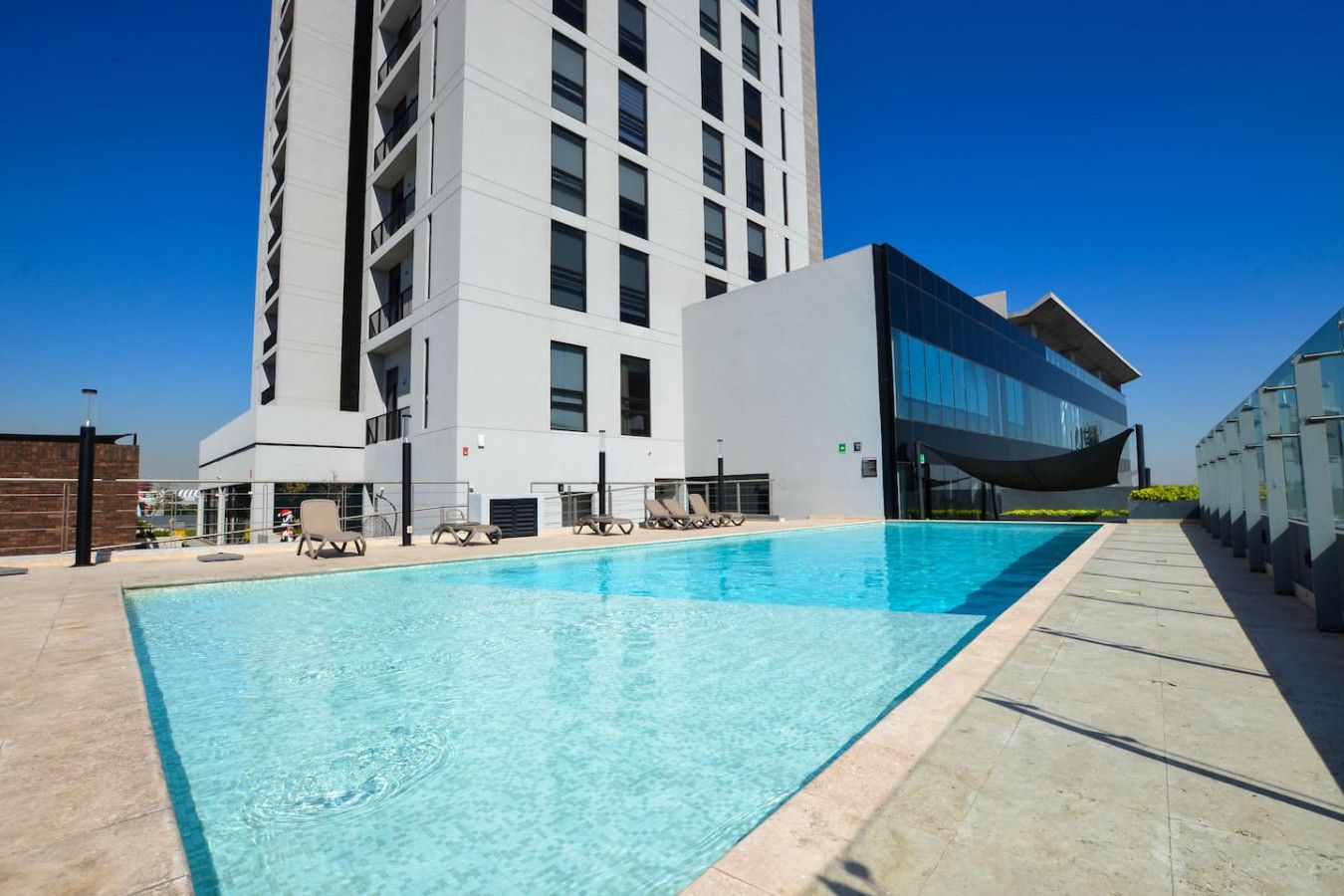A modern hotel with a swimming pool, lounge chairs, and a tall building in the background.
