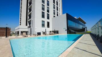 A modern hotel with a swimming pool, lounge chairs, and a tall building in the background.