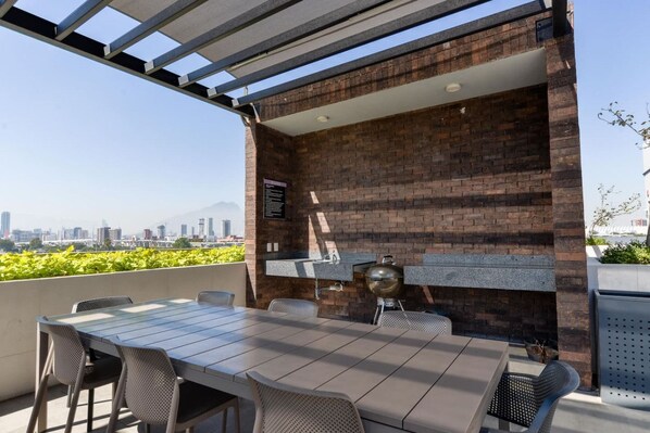 Une terrasse extérieure avec un mur en briques, un barbecue et une table avec des chaises.