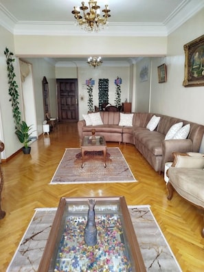 Een ruime woonkamer met een grote hoekbank, een bijzettafeltje en een decoratieve vaas als middelpunt.