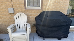 A white plastic chair and a black grill cover against a brick wall. - Fantastic 3-bedroom house with AC in friendly Wichita neighborhood (Wichita)