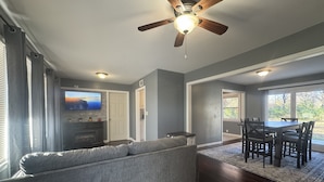 A spacious living room with a gray sectional sofa, a wooden dining table with chairs, a ceiling fan, and a fireplace. - Fantastic 3-bedroom house with AC in friendly Wichita neighborhood (Wichita)