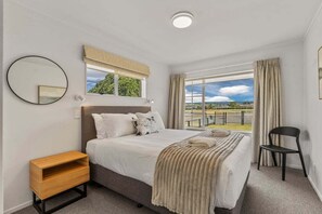 A bedroom with a bed, a nightstand, a chair, and a window with a view. - Park @ Lake Central (Taupo)