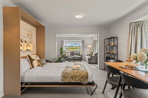 A modern hotel room with a bed, a dining table, and a view of the outdoors. - Park @ Lake Central (Taupo)