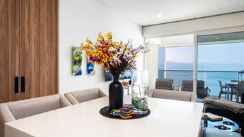 Uma sala de jantar moderna com uma mesa branca, flores coloridas e vista para o mar.