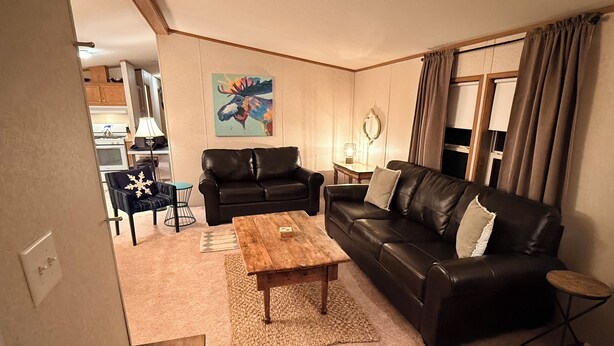 A living room with a black leather sofa, a wooden coffee table, and a painting on the wall. - Charming 3 Bed Room Monthly Rental in the Heart of Ellicottville (Ellicottville)