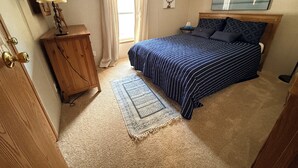 A bedroom with a bed, a nightstand, a lamp, a wooden cabinet, a rug, and a mirror on the wall. - Charming 3 Bed Room Monthly Rental in the Heart of Ellicottville (Ellicottville)