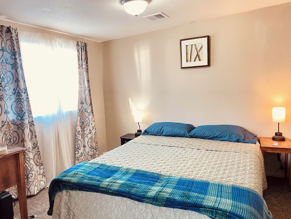 A hotel room with a bed, two bedside tables with lamps, a window with curtains, and a framed picture on the wall.