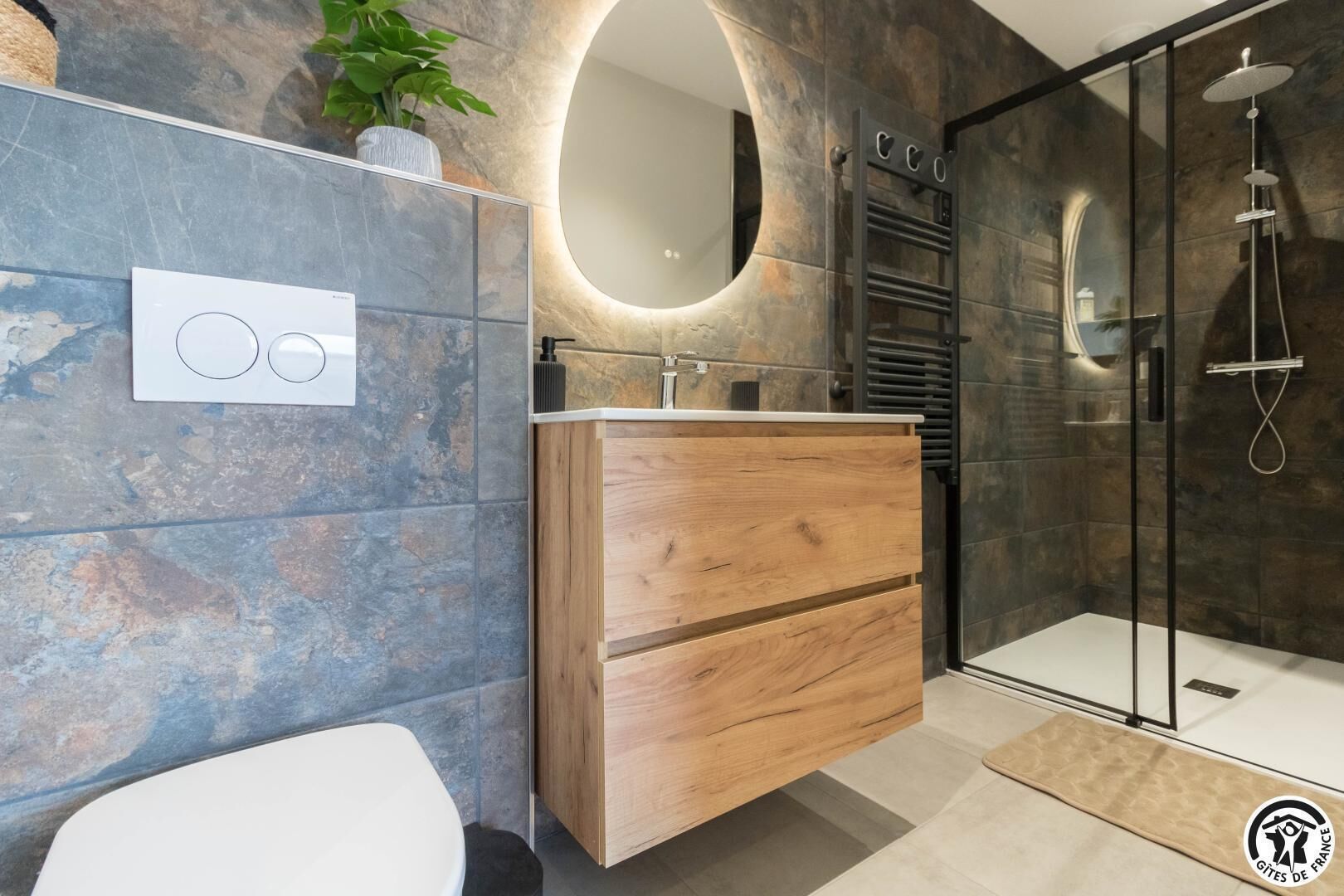 A modern bathroom with a wooden vanity, a glass shower enclosure, and a round mirror.