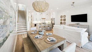 Ein modernes Wohnzimmer mit Esstisch aus Holz, weißem Sofa und einer Kronleuchter.