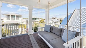 Ein überdachter Balkon mit Schaukelstuhl, weißen Geländern und Blick auf Nachbarhäuser.