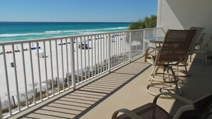 Un balcon avec vue sur la plage et l’océan. On y trouve des chaises et une table.