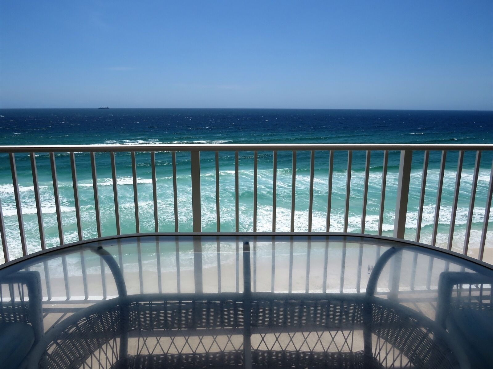 A balcony with a view of the ocean, featuring a glass railing and wicker chairs.