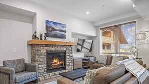 Ein Wohnzimmer mit Kamin aus Stein, Ledersofas, einem Couchtisch und einem großen Fenster mit Jalousien.