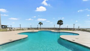 Una piscina limpia con borde curvo, rodeada de una valla y palmeras.