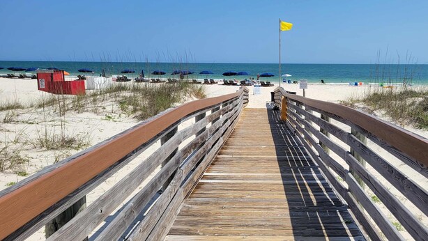 Un paseo marítimo de madera que conduce a una playa con sombrillas y una estación de salvavidas.