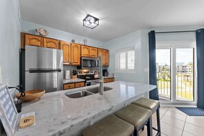 A modern kitchen with wooden cabinets, stainless steel appliances, a marble countertop, and a view of the outdoors. - Gulf View Condo, Pools, Hot Tubs (Gulf Shores)