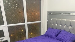 A bed with a purple bedspread and matching pillows, a grey upholstered headboard, and a window with a view of trees. - 2 bedroom 2 bathroom condominium downtown Toronto (Toronto)