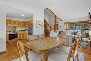Eine geräumige Küche mit Holzschränken, einem Esstisch mit Stühlen, einem Kühlschrank und einem Herd. Eine Treppe führt zu einem Wohnbereich mit einer Couch und einem Fernseher.