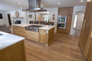A modern kitchen with a large island, built-in oven, and stainless steel range hood. - Spacious 5-bedroom house in gorgeous, convenient Avon with pool and fitness room (Avon)