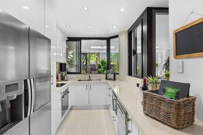 A modern kitchen with stainless steel appliances, a large window, and a wicker basket with a book. - Luxury Beachfront Apartment with Direct Pool Access (Cairns)
