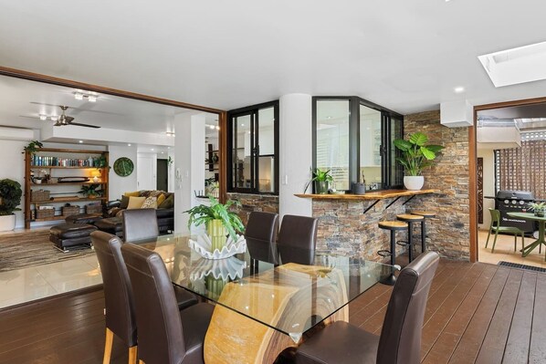 A modern dining area with a glass table, leather chairs, and a stone accent wall. - Luxury Beachfront Apartment with Direct Pool Access (Cairns)