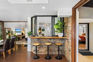A modern living room with a dining area, a kitchen, and a bar area with stools. - Luxury Beachfront Apartment with Direct Pool Access (Cairns)