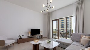 Een moderne woonkamer met een bank, een salontafel, een televisie en een balkon met uitzicht op gebouwen.