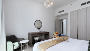 Een moderne hotelkamer met een groot bed, een bureau met spiegel, een kleine fauteuil en een nachtkastje met een schaal fruit.