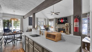 A modern kitchen with a large island, a fireplace, and a dining area with a view of the outdoors.