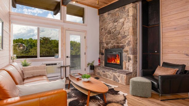 A modern living room with a stone fireplace, leather furniture, and a large window offering a view of the outdoors. - Sunset Ridge (#338) | Walk to Ski Bike Eat! (Basye)